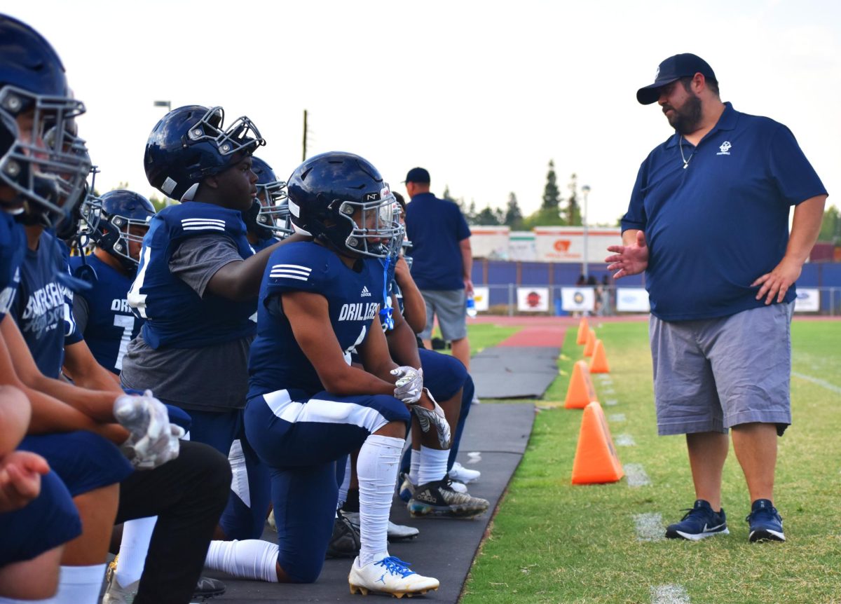 The football players receive feedback from a coach on the sidelines.